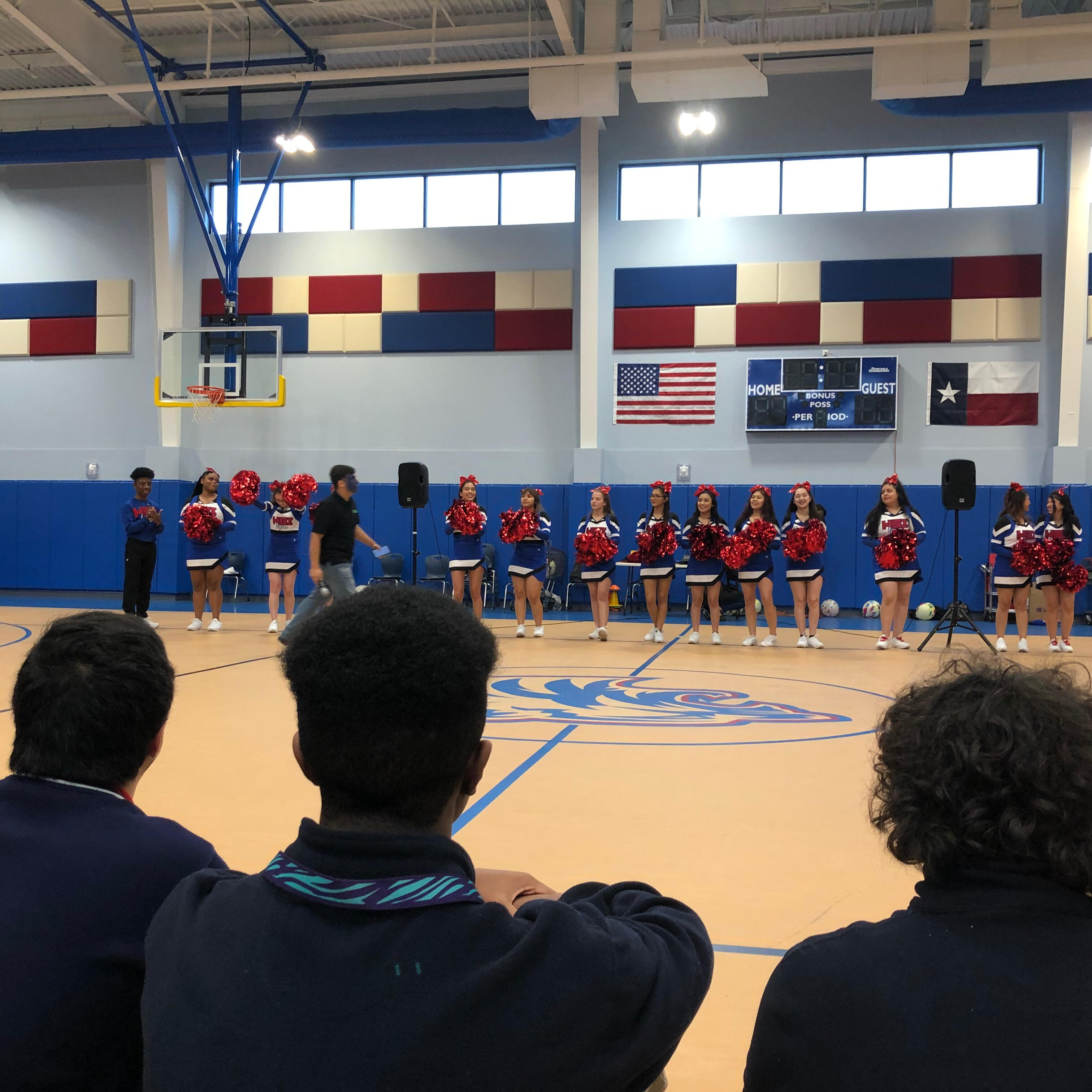 Image students on gym bleachers watching the cheerleaders perform during halftime at a school basketball game.